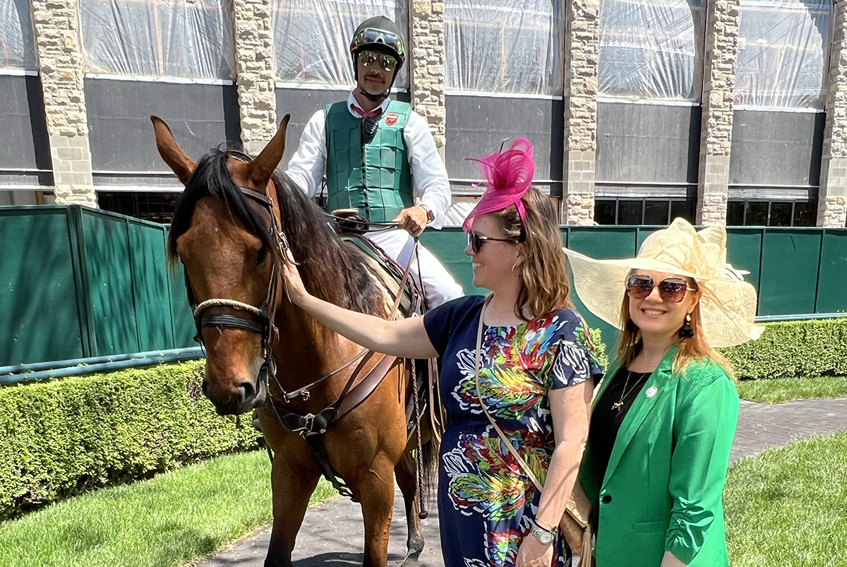 women smiling and petting a horse that has a jockey rider